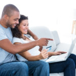 Couple enjoying online shopping sitting on sofa at home